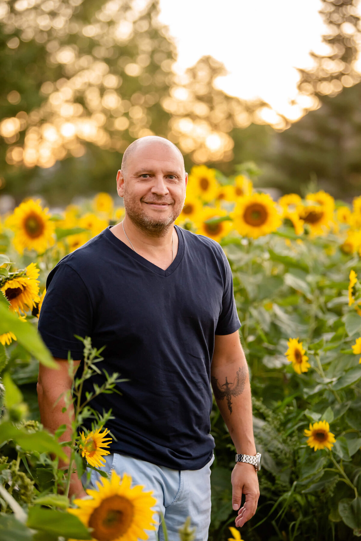 Dad wearing a navy blue shirt standing in a sunflower field for his family photos