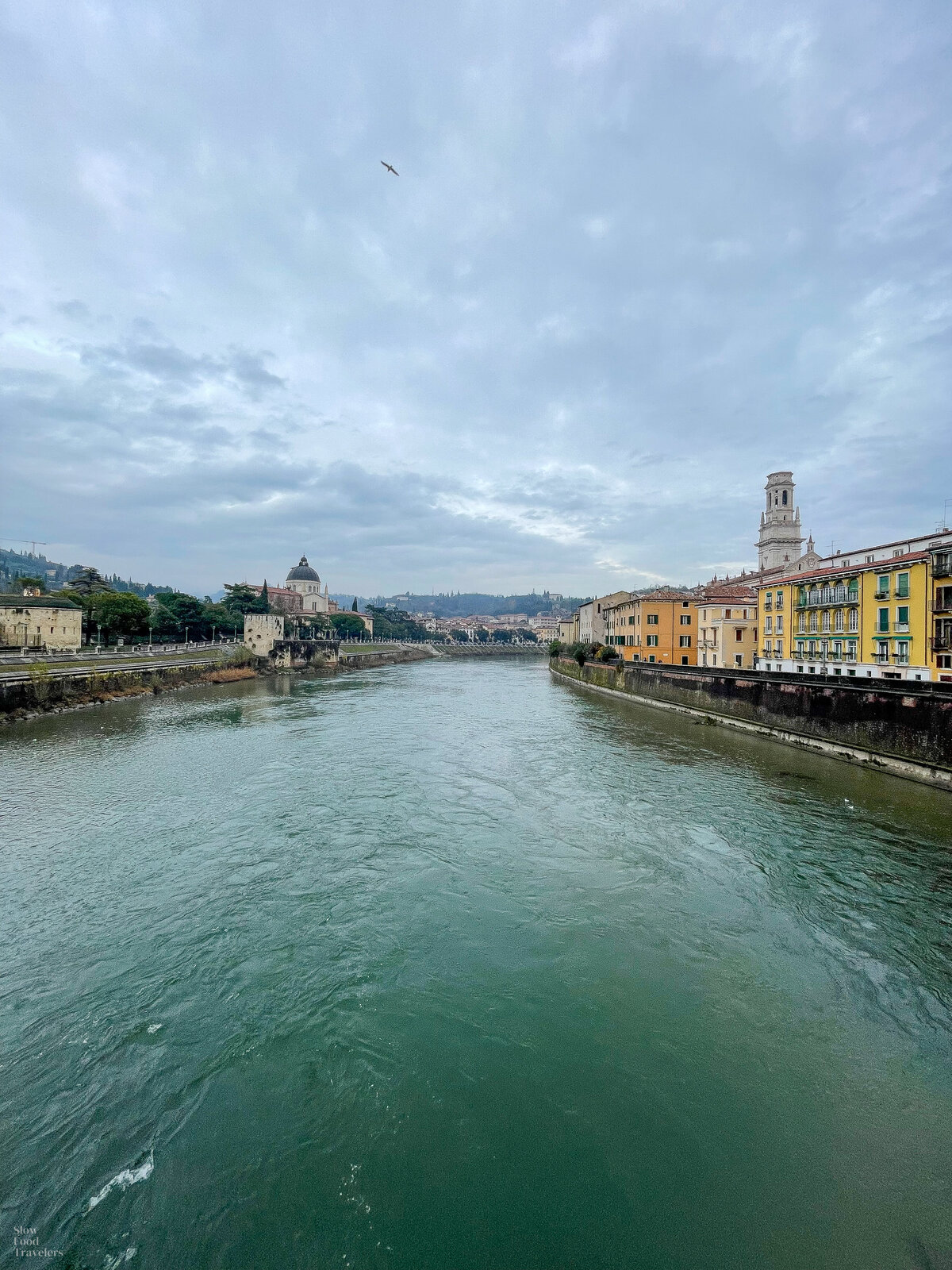 A view of the verona cityscape with the Adige river in the foreground and moody clouds in the background.