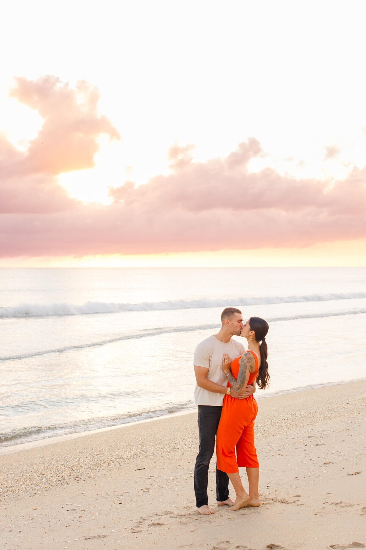 Couple stands near the shoreline kissing at sunrise