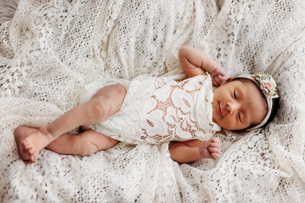 newborn baby girl wearing a lace outfit laying on a pile of vintage white lace.