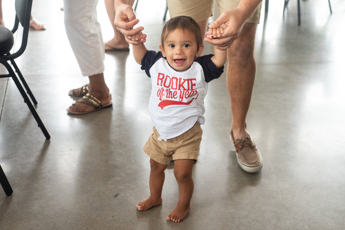 smiling baby wears rookie of the year shirt holding dads hands