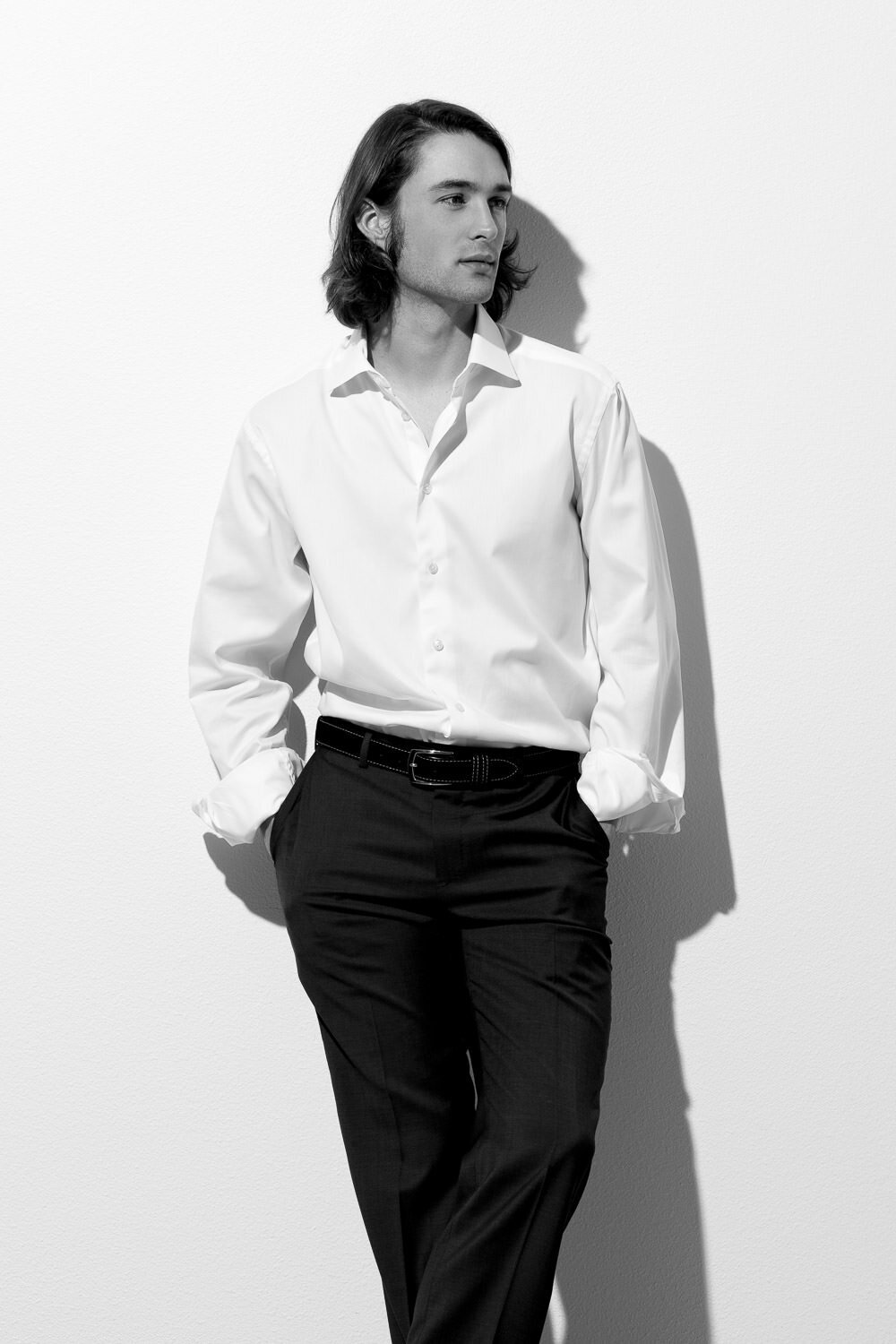 Editorial-style headshot of a man in slacks and a button-down shirt with rolled sleeves against a white wall in Austin, TX