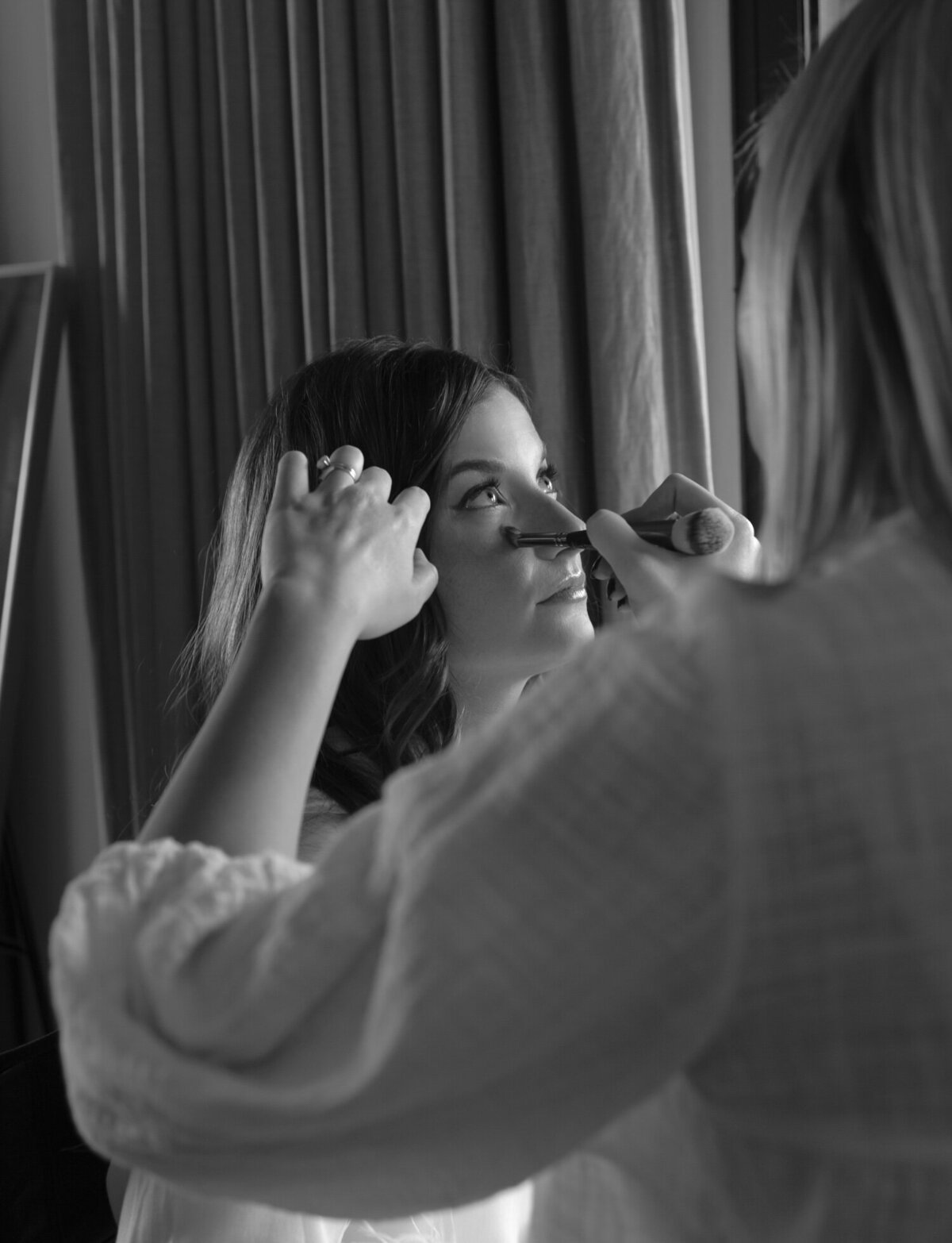 A bride gazes up, light sparkling of her eye while getting her makeup done at Shinola Hotel