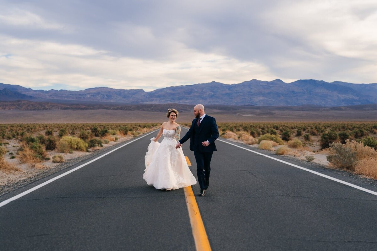 An enchanting elopement moment at Death Valley National Park, as the couple runs happily down the open road, celebrating their love and adventure.