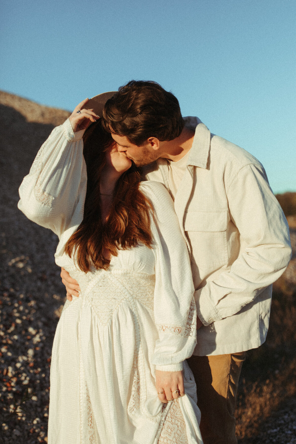 Boho couple in all white outfits are kissing.