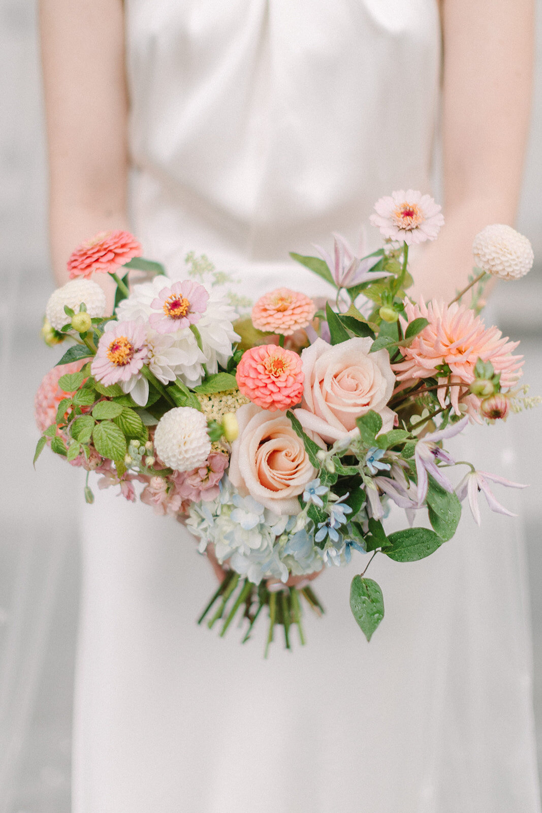 A bride holds a garden style bouquet of pink roses and zinnias at a Montreal wedding.