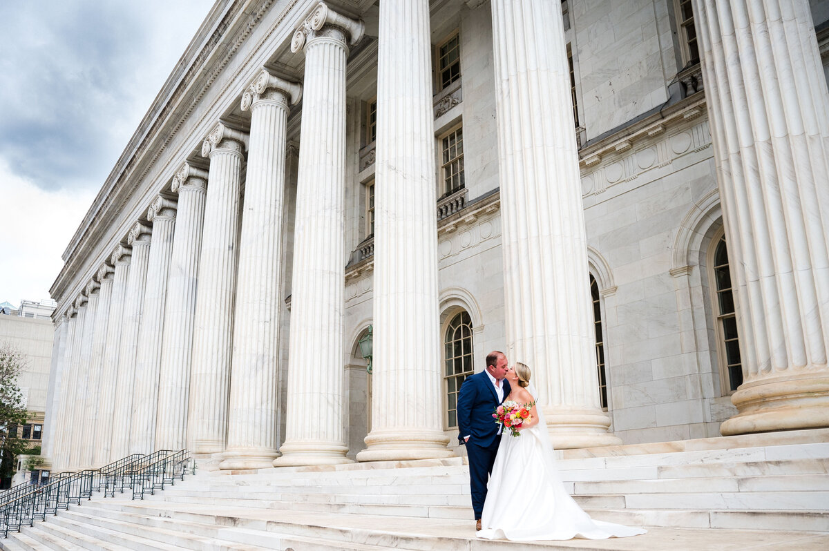 A bride and groom share a kiss on the steps of a downtown Denver building.