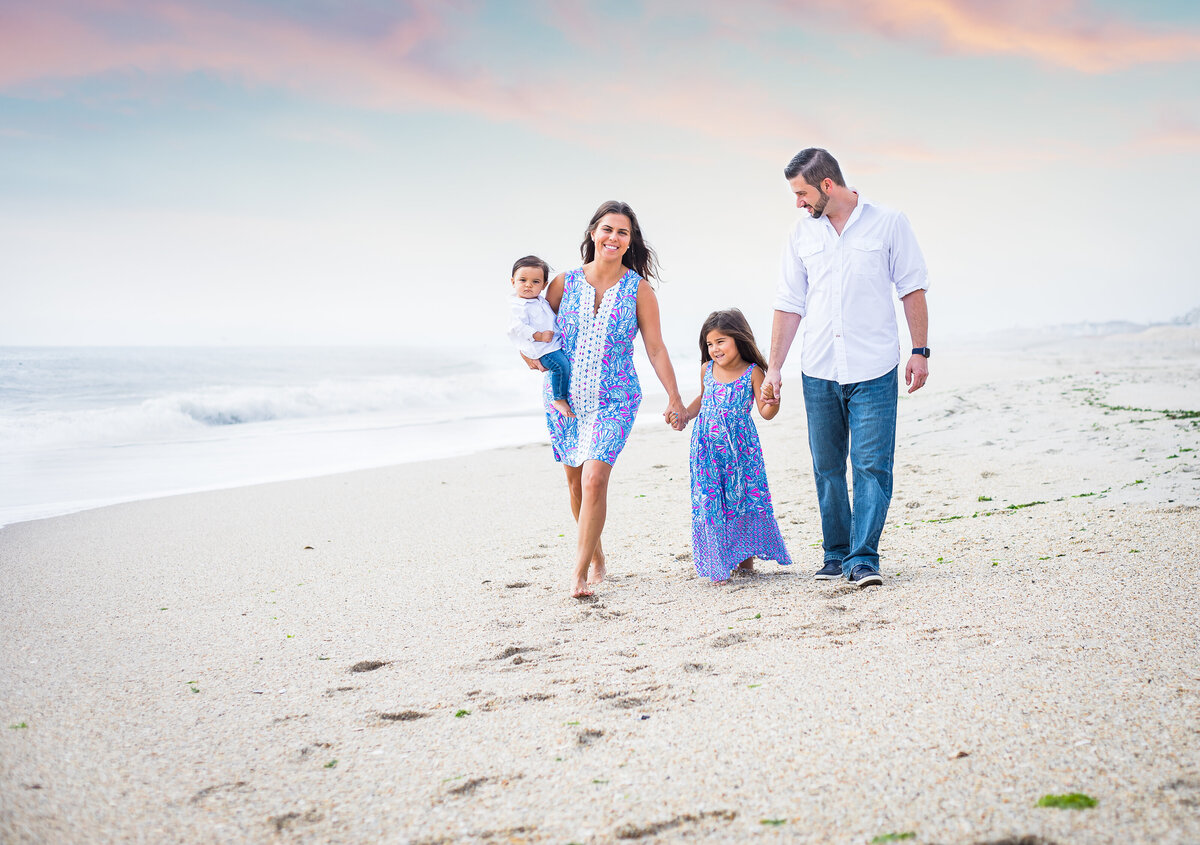 family with young kids walking down beach holding hands and smiling at each other