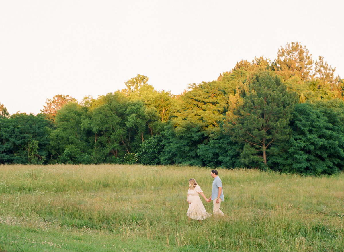 New parents walk through a field at the NC Art Museum during their maternity session. Image by Raleigh maternity photographer A.J. Dunlap Photography.