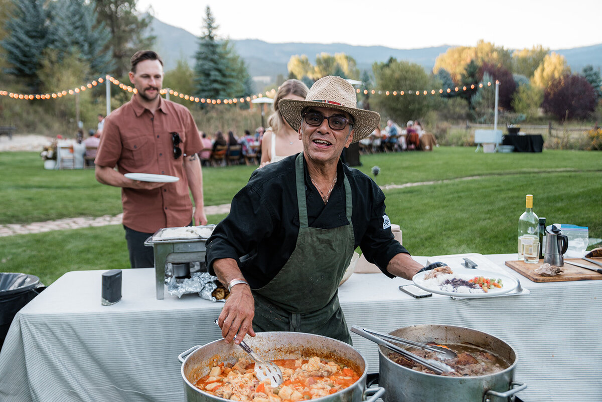 A man in a hat serves food at a wedding.