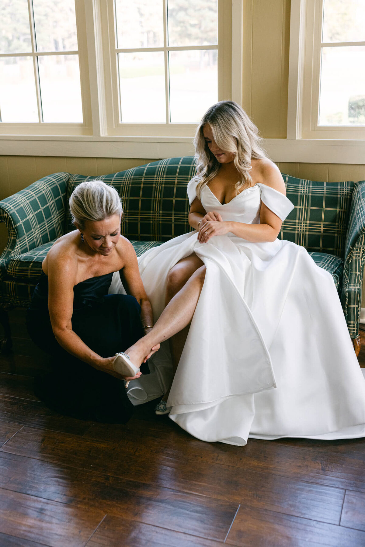 A wedding day photo of the brides mom putting helping the bride put on her shoes