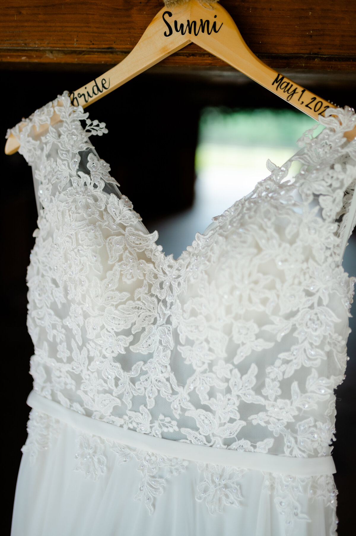 lace wedding dress hanging on a wood hanger in a doorway with the brides name and wedding day date