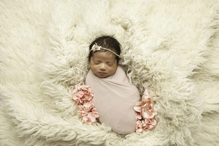 Newborn baby girl snugly wrapped, surrounded by delicate flowers, creating a soft and dreamy floral-themed portrait
