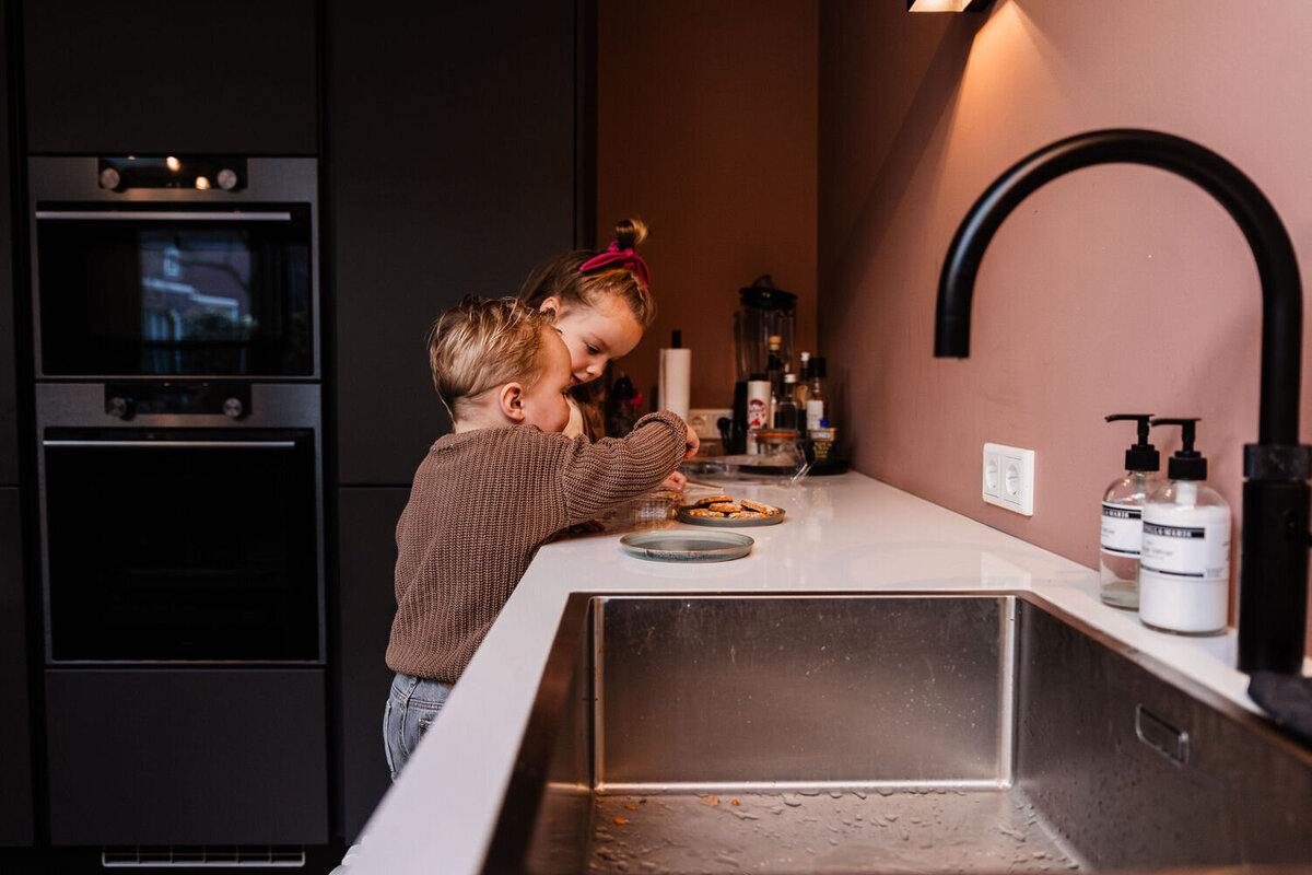 Meisje en jongen staan aan aanrecht en leggen koekjes op een schaaltje