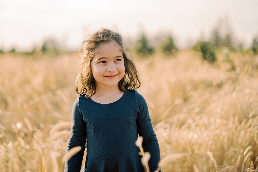 Toddler girl standing in a field of yellow grass at a Christmas tree farm