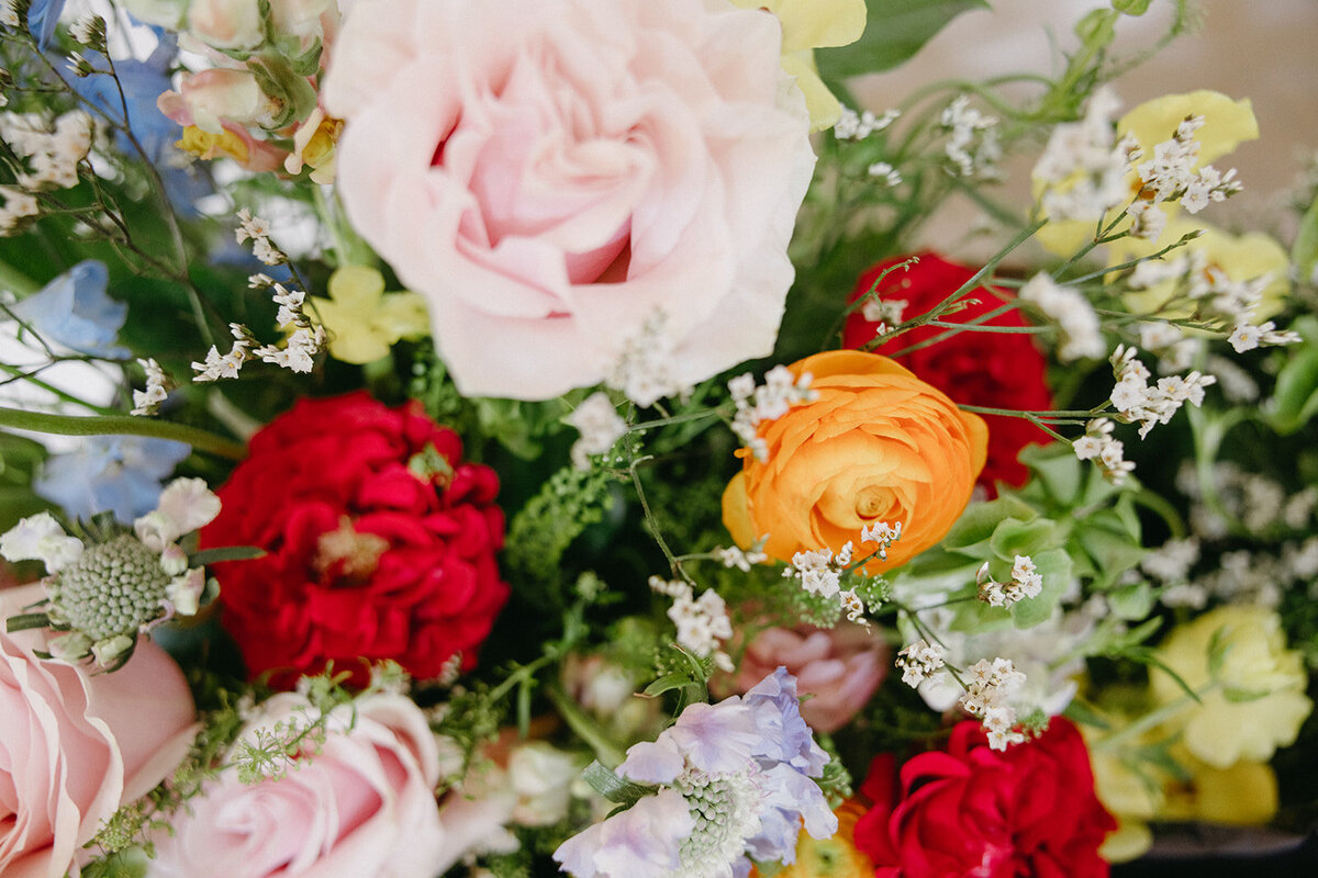 Close-up of soft pastel bouquet featuring blush, cream, and red and orange flowers. 