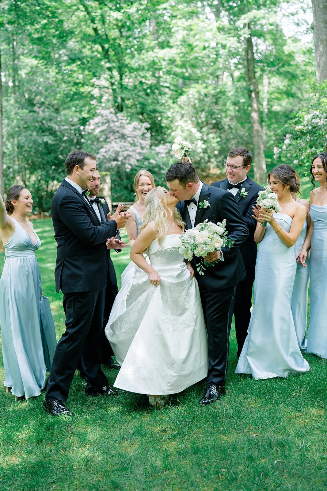 Bride and groom kissing while the wedding party cheers around them during outdoor wedding photos in Highlands, North Carolina.