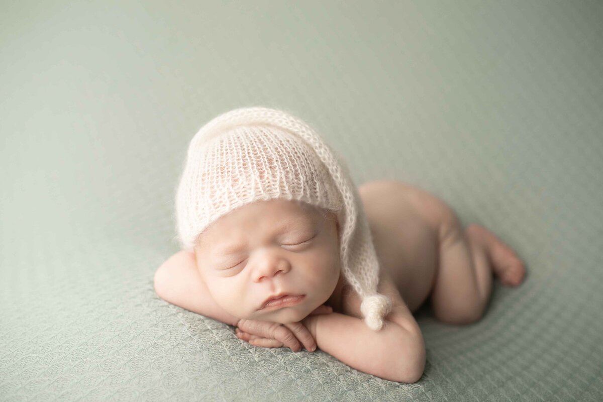 Newborn baby boy with fiery red locks curled up on a plush backdrop, his delicate features highlighted in soft lighting