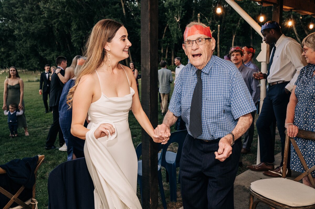 candid photo of a bride dancing with elderly grandfather on wedding day outside on lawn at orton bradley park charteris bay