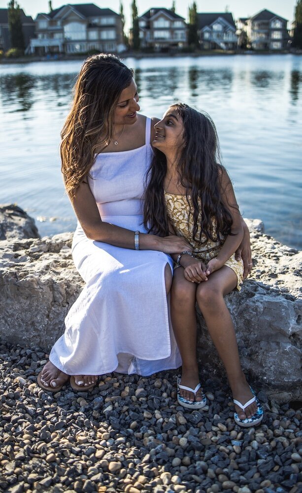 A mom and daughter sit side by side on a rock by the lake