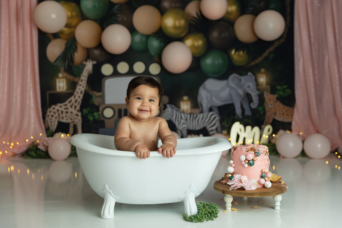 A toddler girl smiles while sitting in a small bathtub in a studio of a New Jersey Milestone Photographer