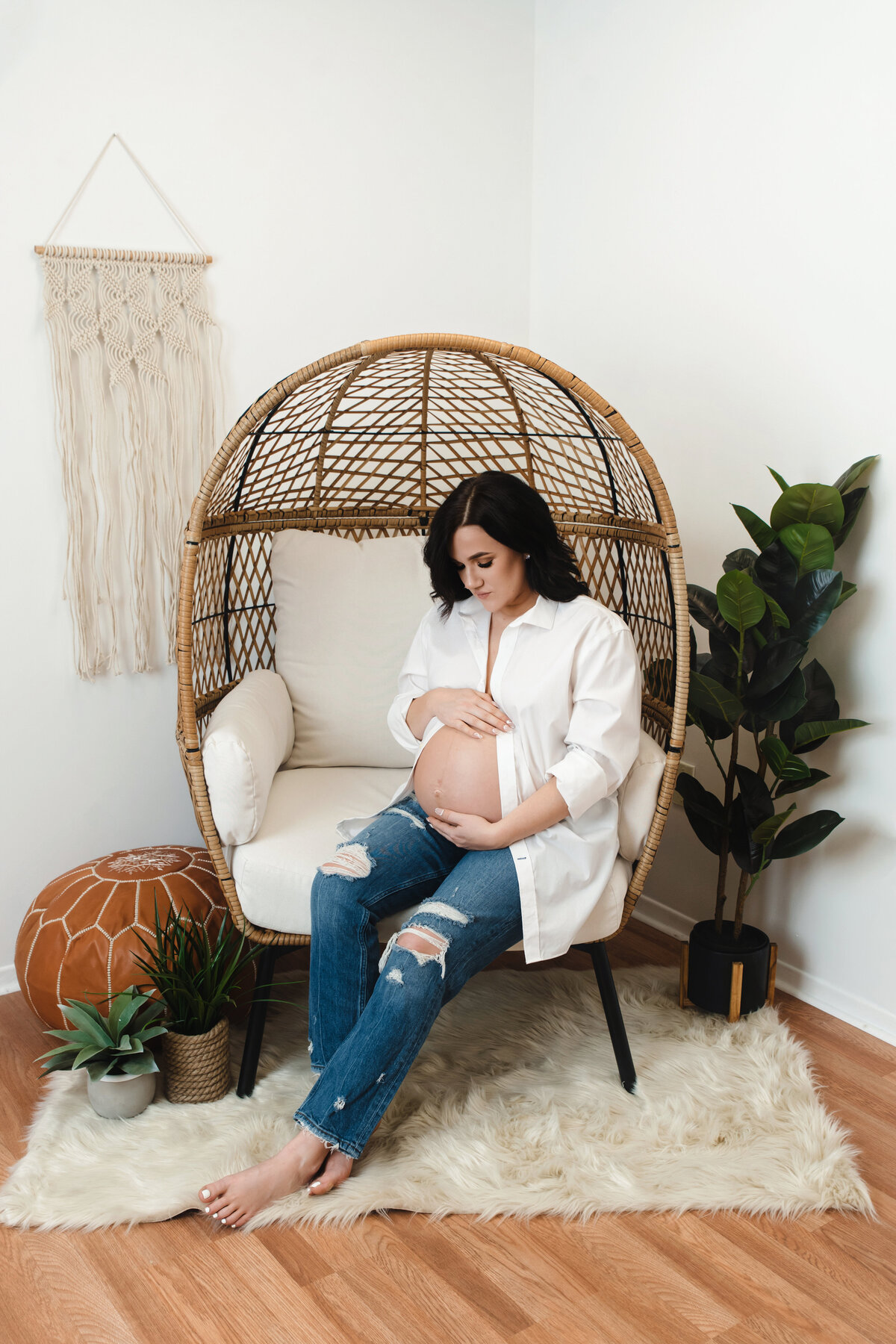 pregnant mom with jeans and white shirt sits on egg chair with boho setup