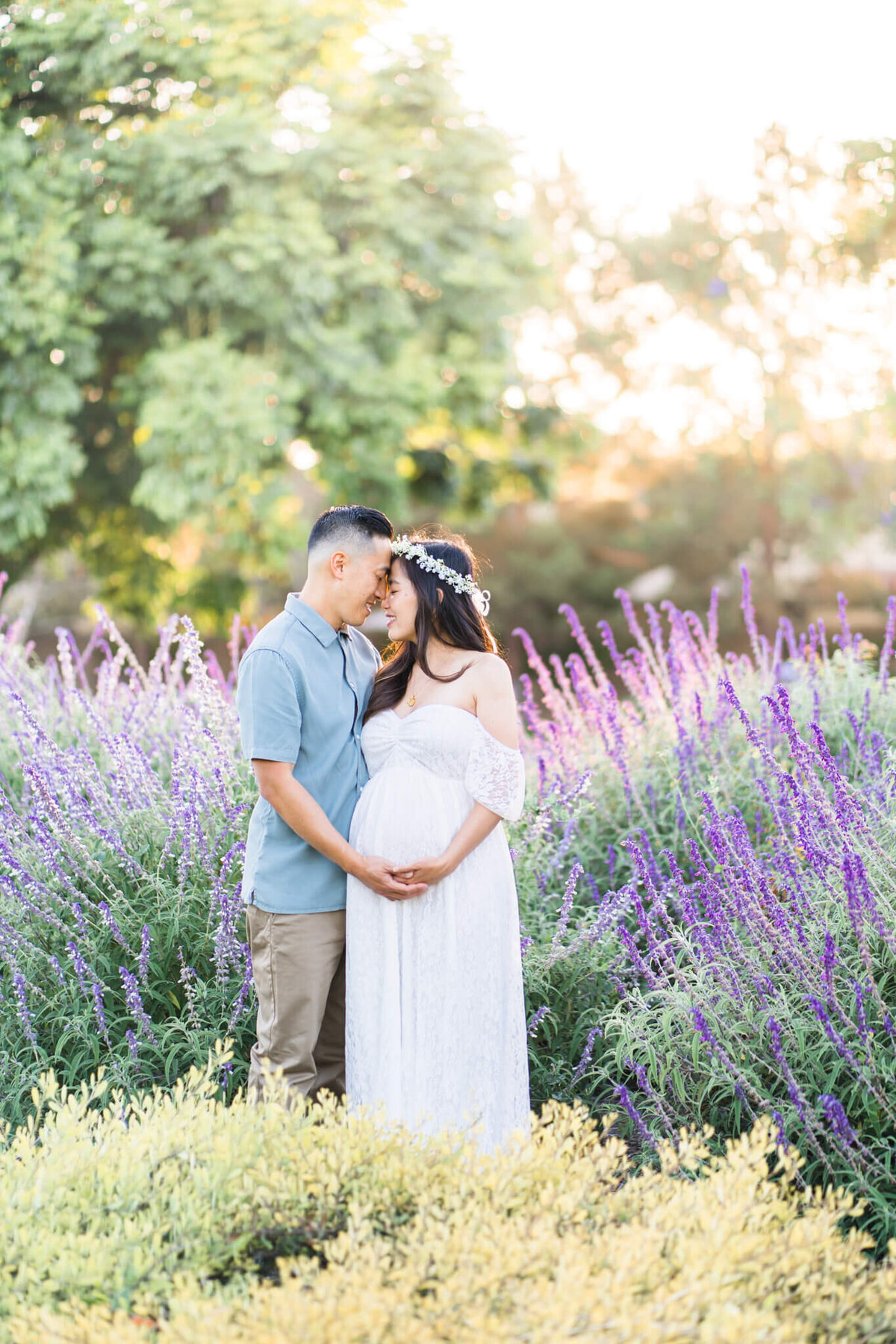 Pregnant couple with white flower wreath standing in a field of purple flowers