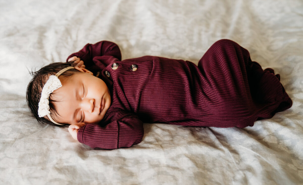 Newborn Photographer, a baby girl in a onesie sleeps on parents bed