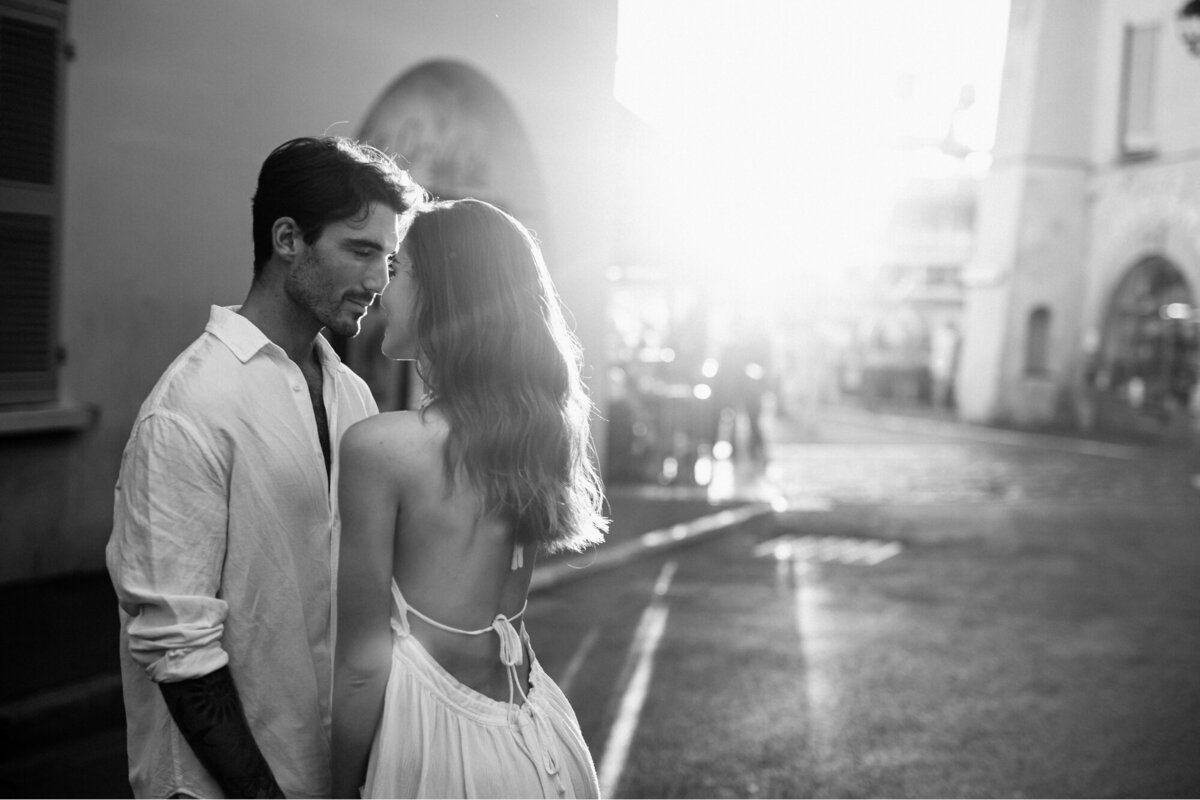 Black and white photo of a Couple about to kiss with the sun going down behind them shining down on them.