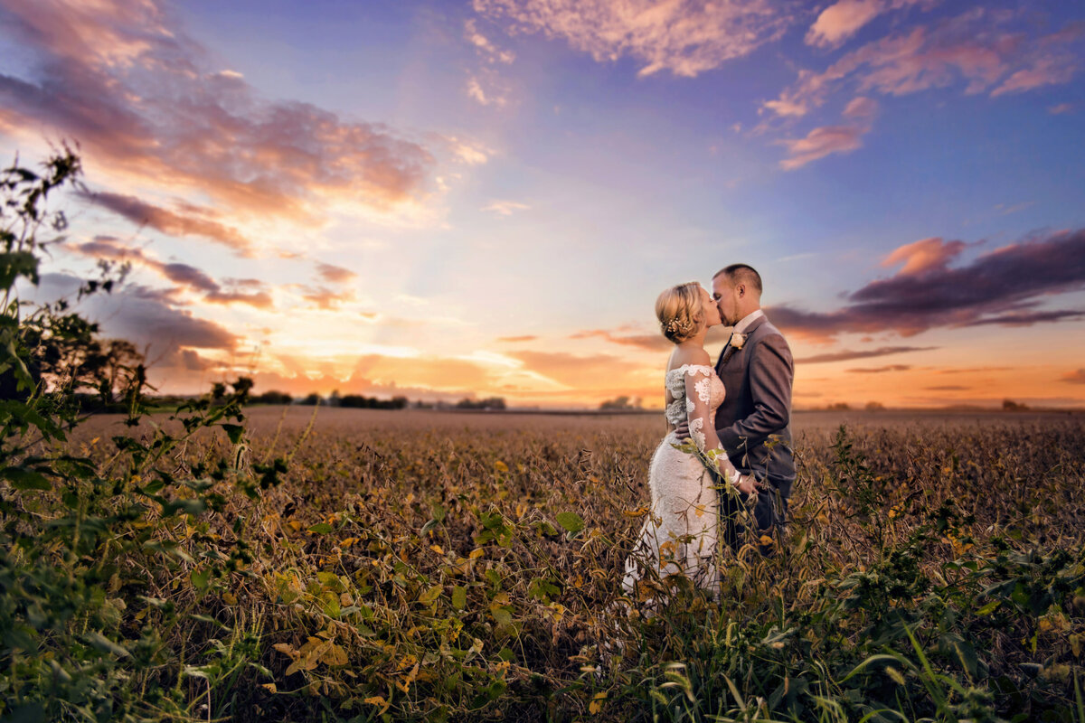 Beautiful bride and groom kiss on their wedding day in a field at sunset