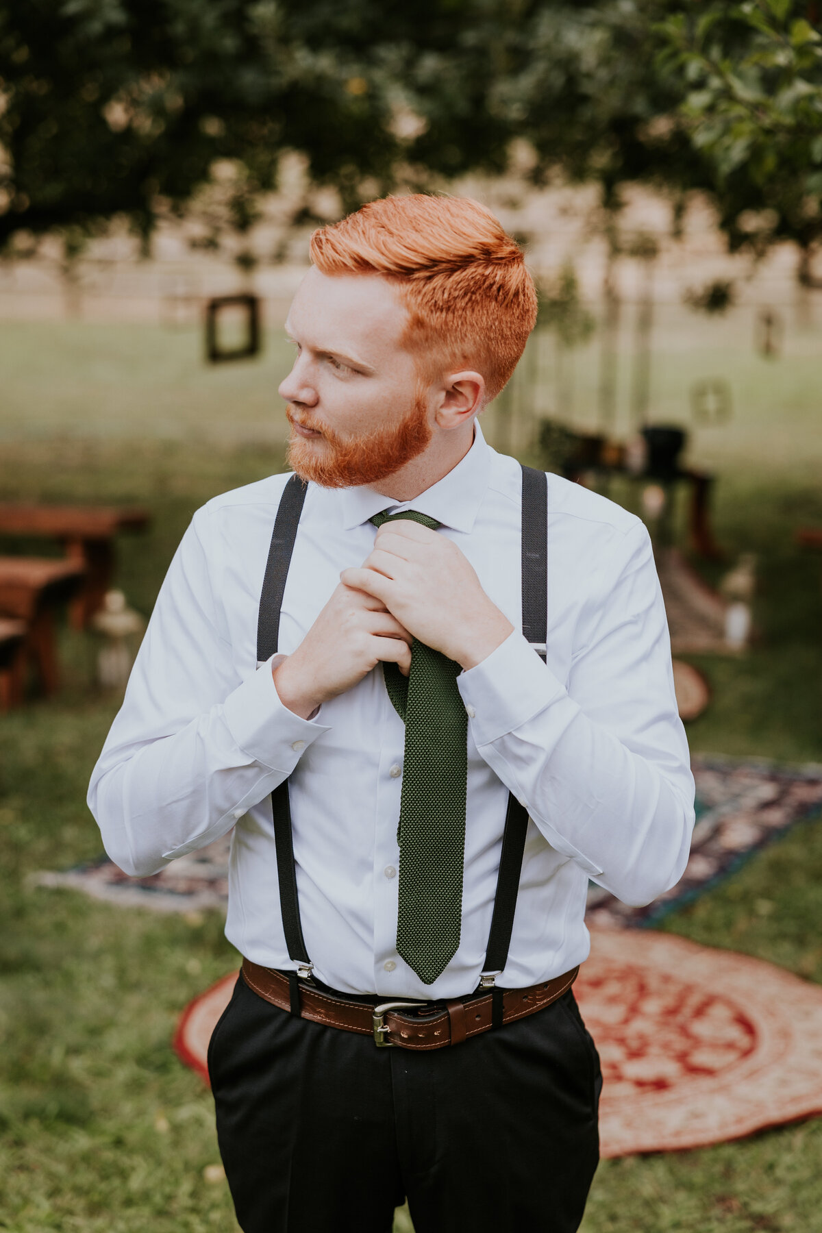 Groom adjusts tie while looking to the right on the camera frame.
