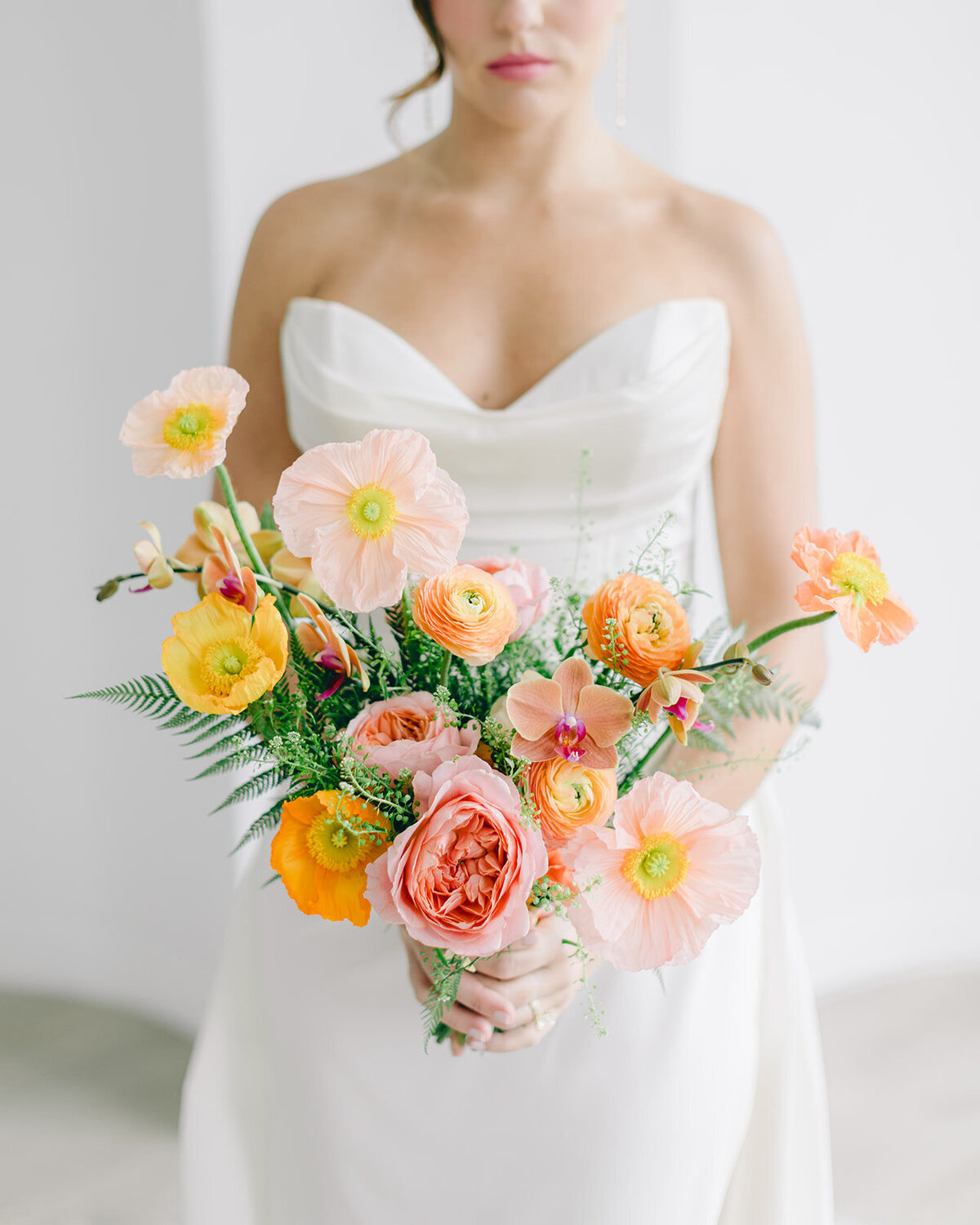 A bride in a strapless dress holds a colorful bouquet of bright spring flowers. 