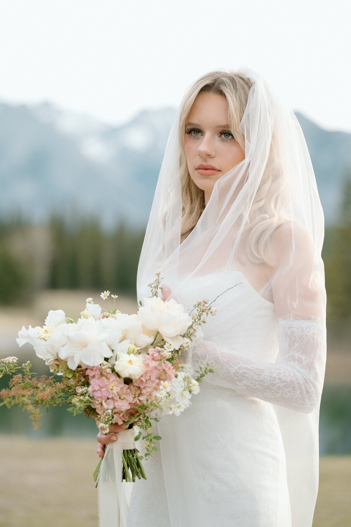 Bride holding floral bouquet with dramatic mountains behind her at Banff wedding.