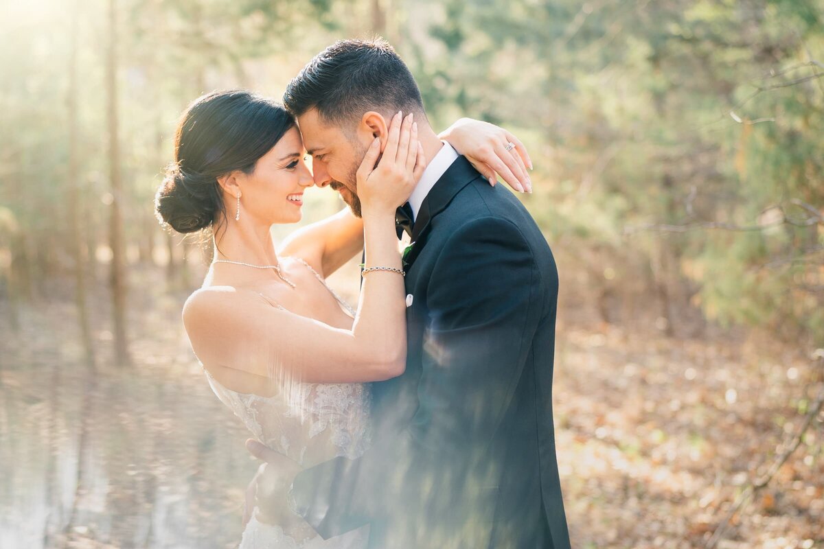 wedding couple standing in a wooded area about to kiss.