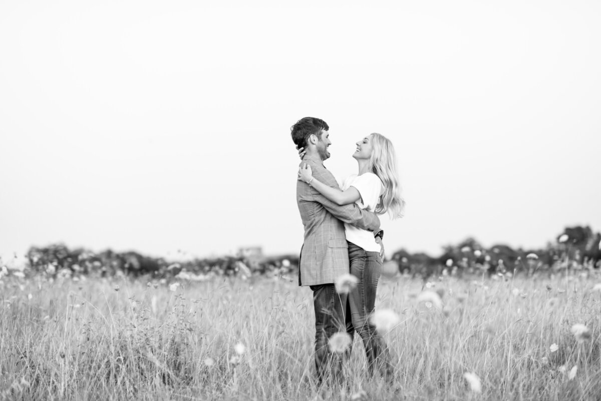 Engagement pictures at white rock lake. Couple shares a laugh in a field full of wild flowers.