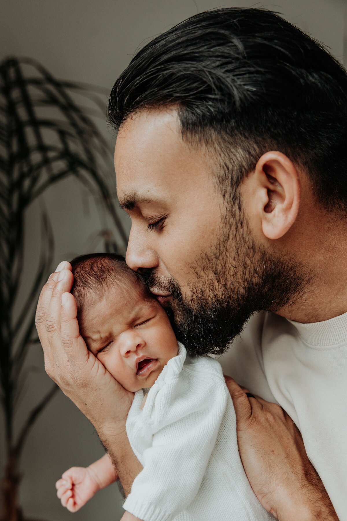 Dad holds newborn baby on his arm and kisses on the side of the head