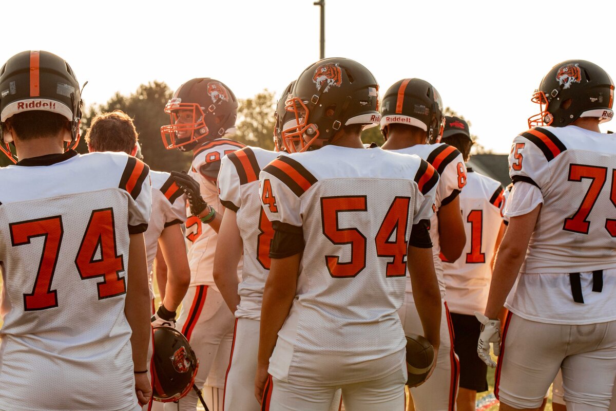 Photo of a group of football players from behind standing on the sidelines