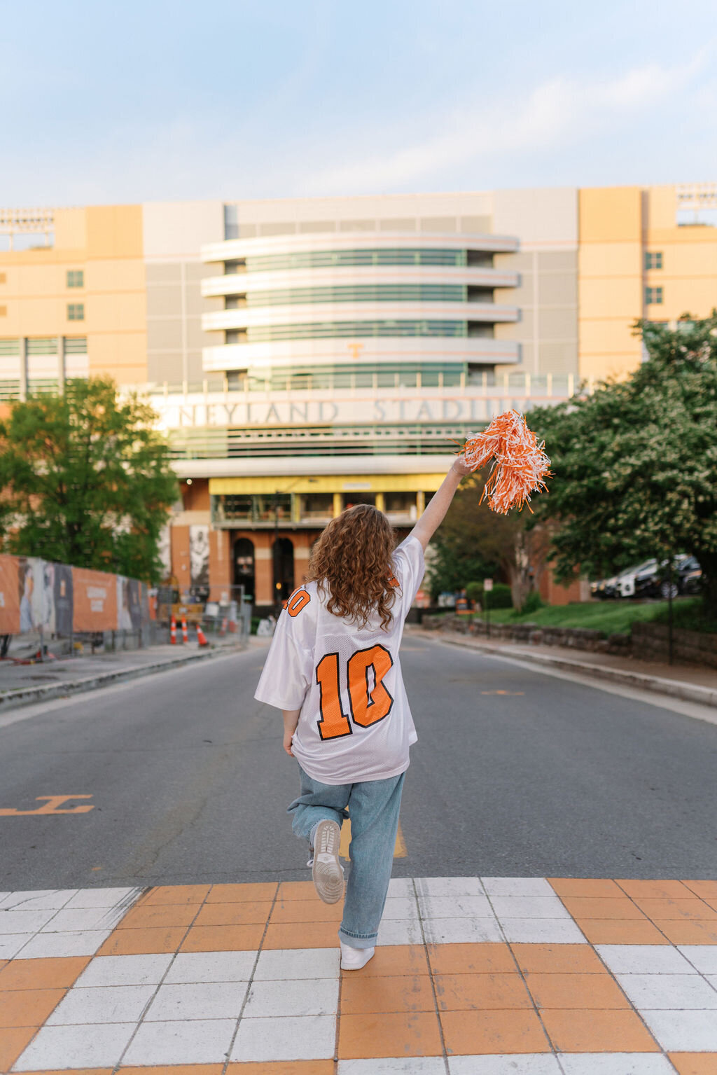 girl in white and orange volunteers jersey waves pom pom in front of neyland stadium in knoxville tennessee