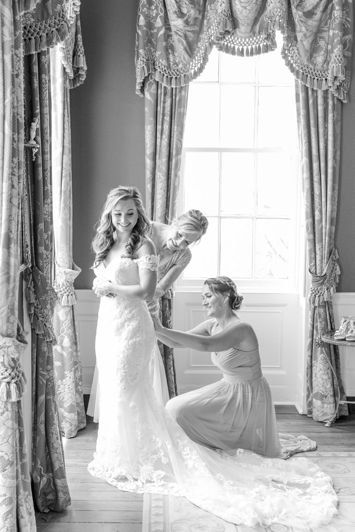 bride gets into dress with mother and sister