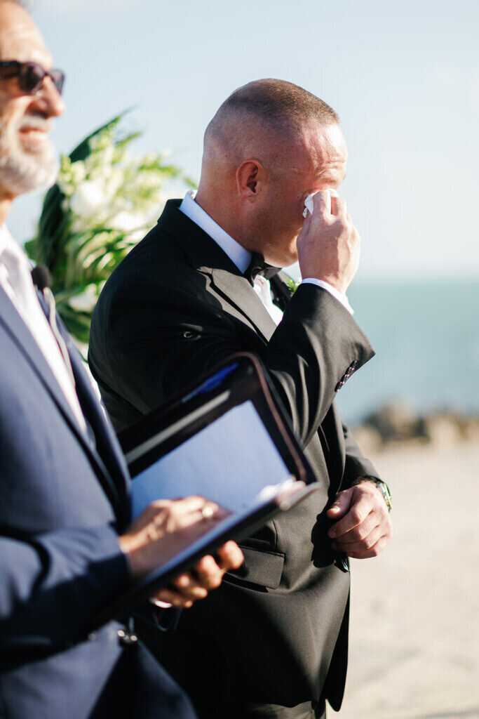  A touching moment as the groom wipes away tears while waiting for his bride at their beachfront ceremony. Captured by Claudia Amalia Photography, a Florida Keys wedding photographer.
