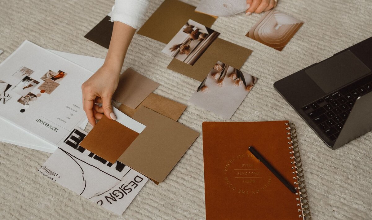 Vickie of VERVE & COLOR arranging pieces for a moodboard with a notebook and laptop nearby, creating a grounded and thoughtful experience