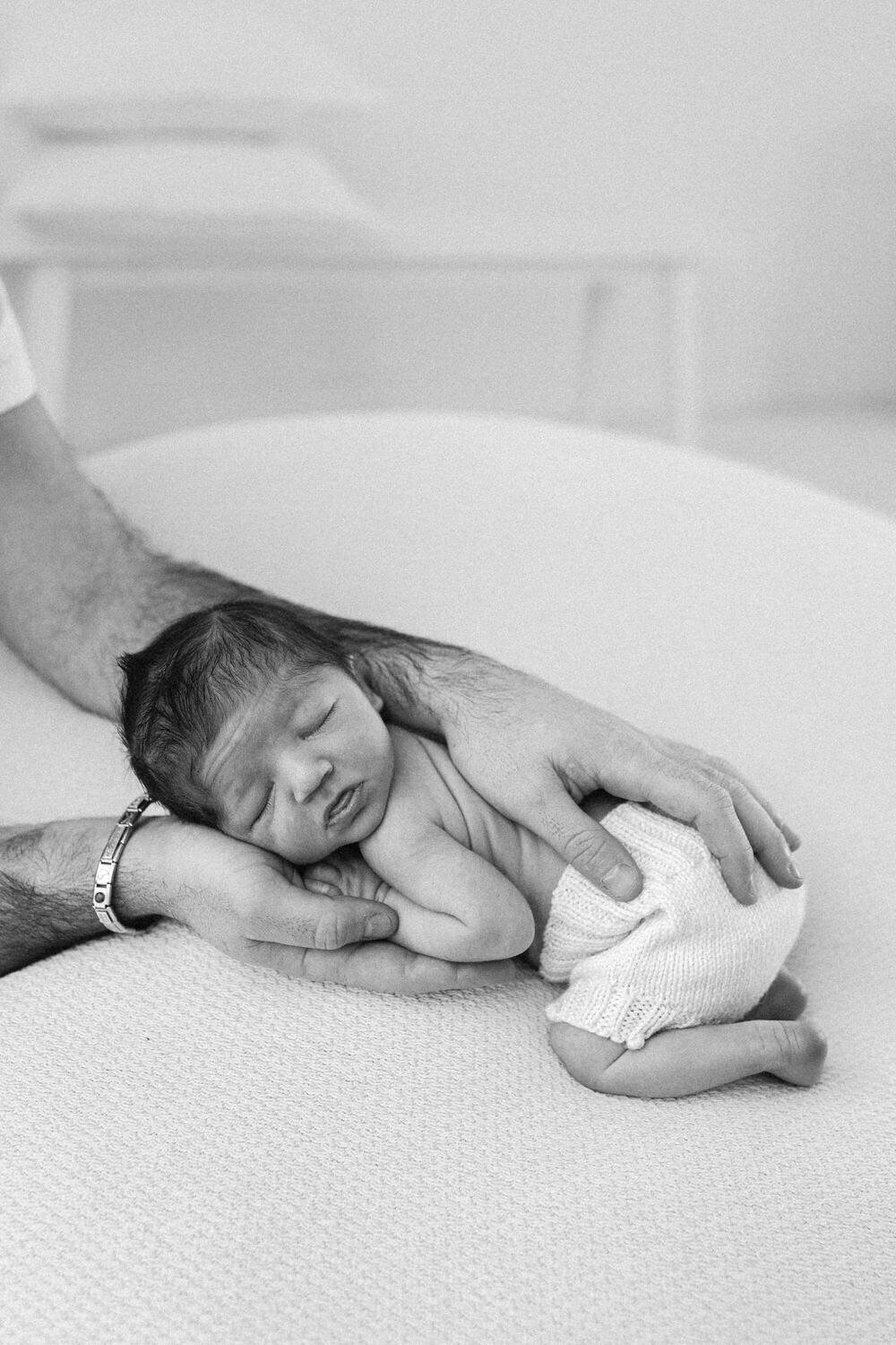 baby held in dads hand whilst they sleep