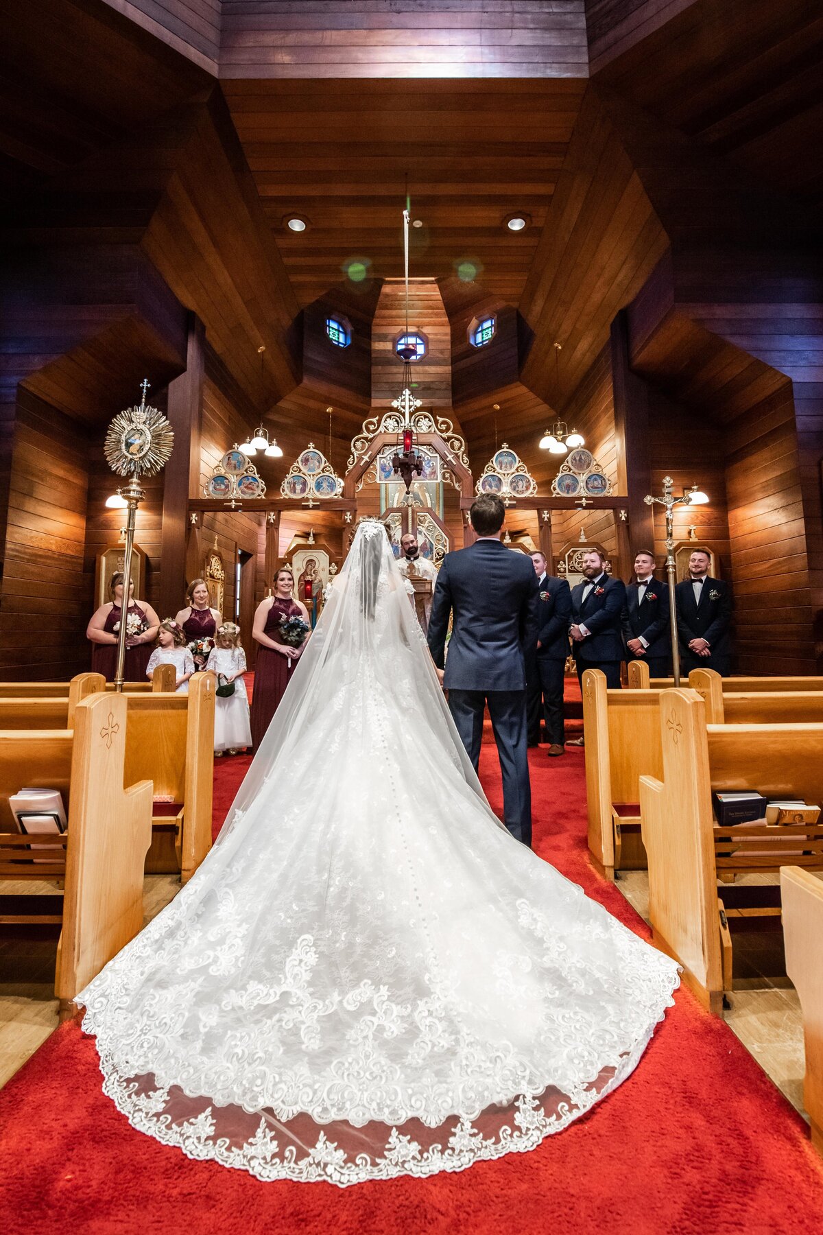 a photo of the back of a bride's dress as she walks down the aisle of  a church