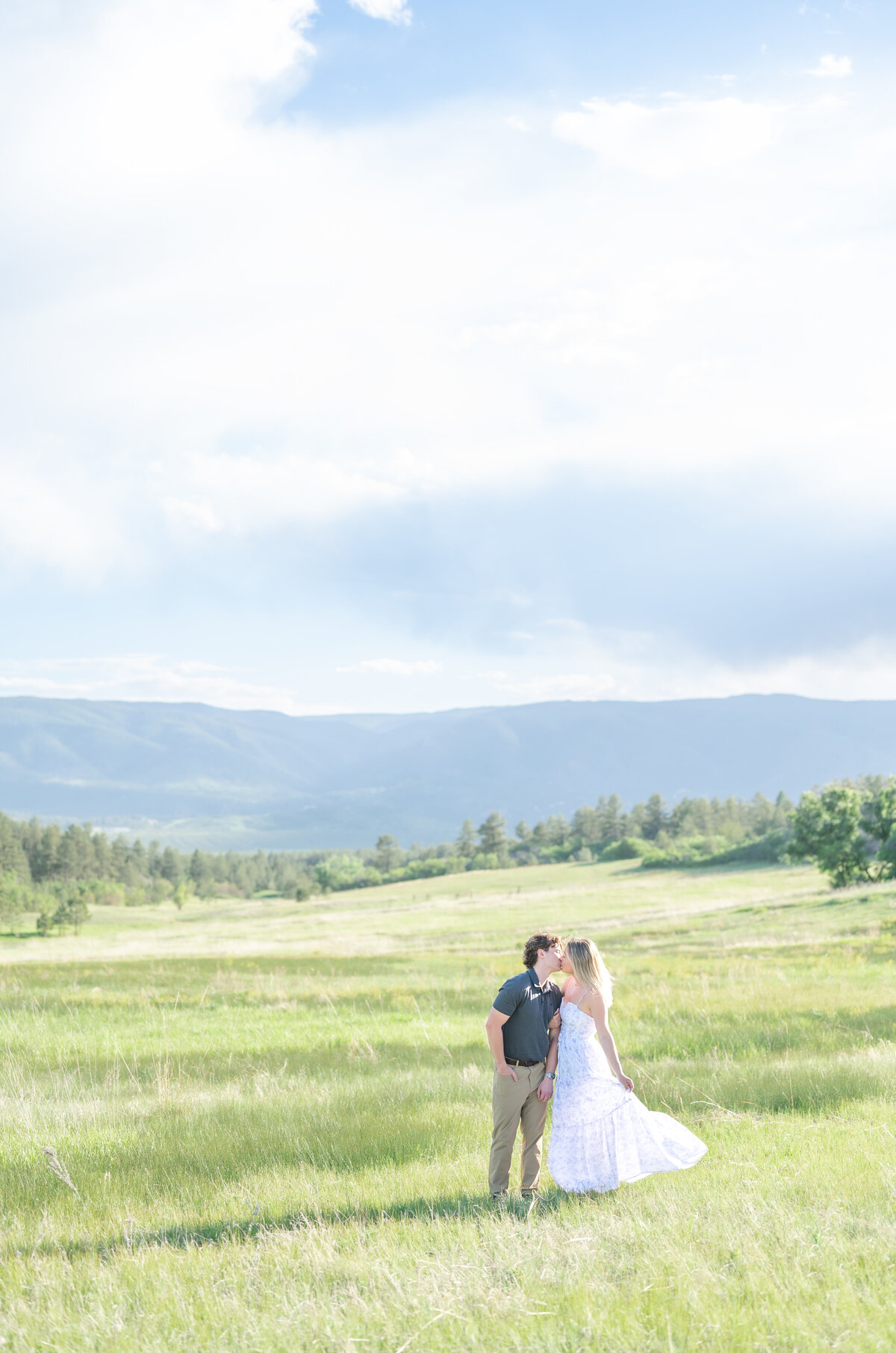 Couple kissing in an open meadow field with the mountains behind them