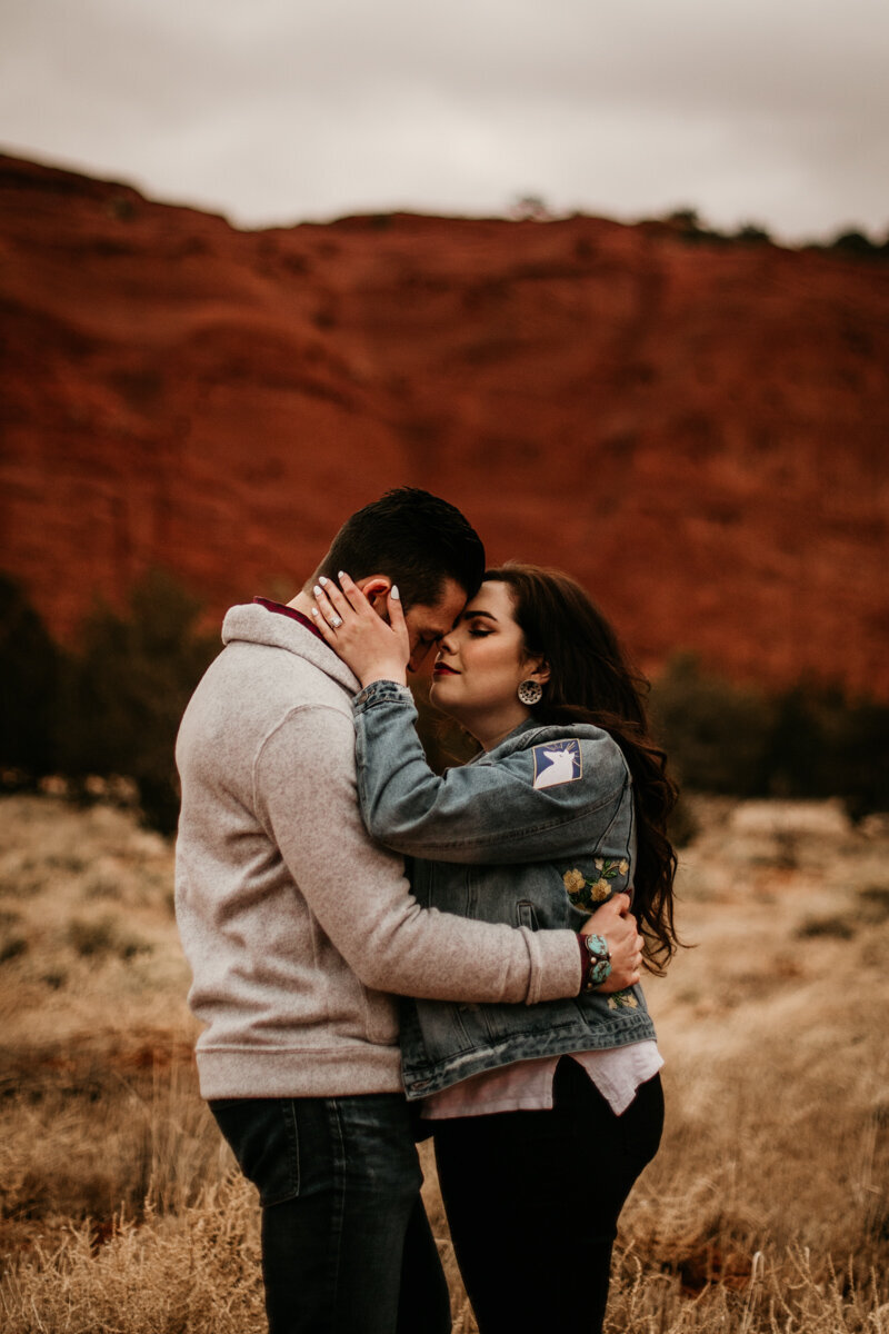 engaged couple about to kiss in front of red rocks