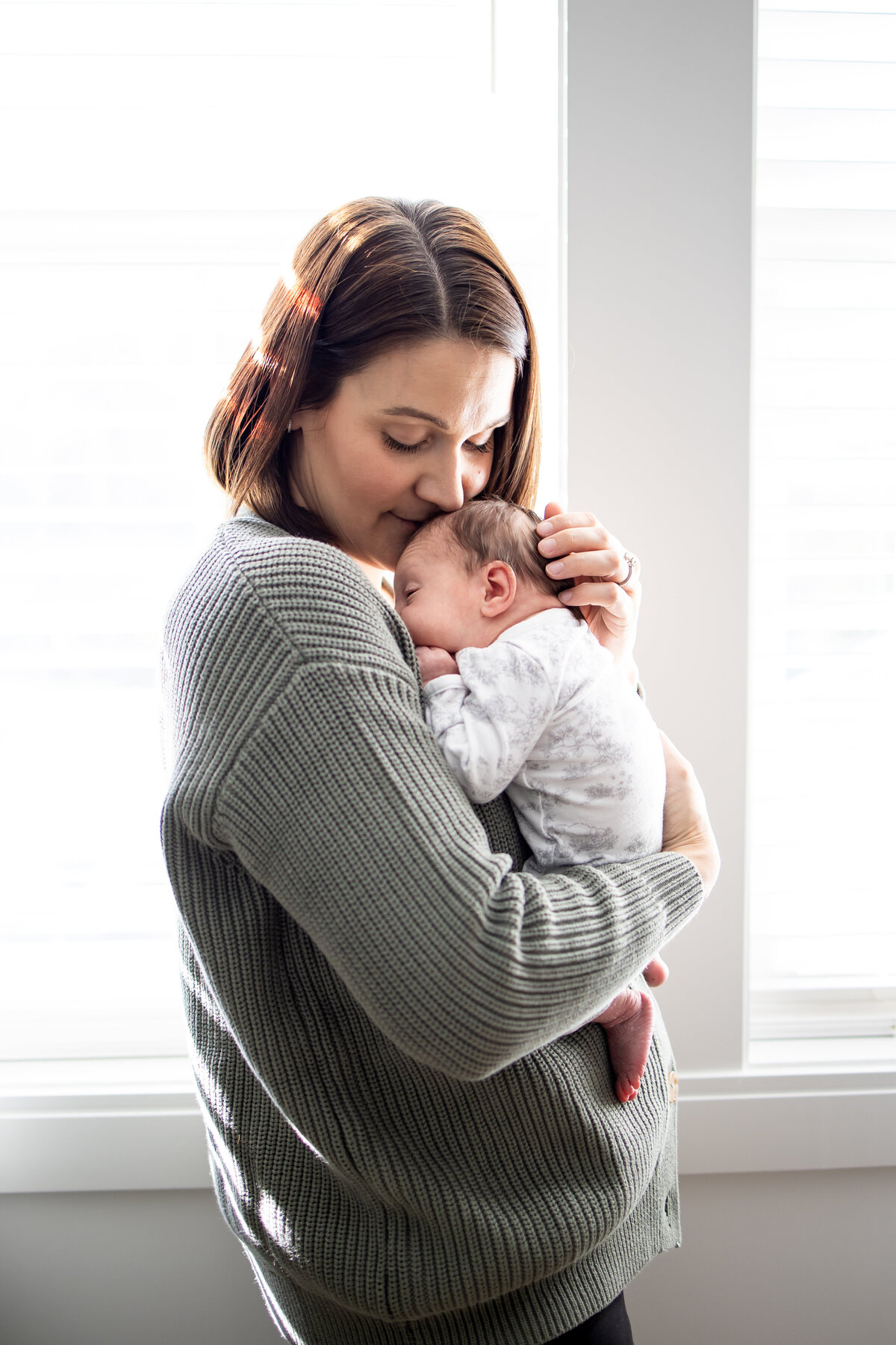 Mom holding newborn baby in front of windows in the nursery in Wayland