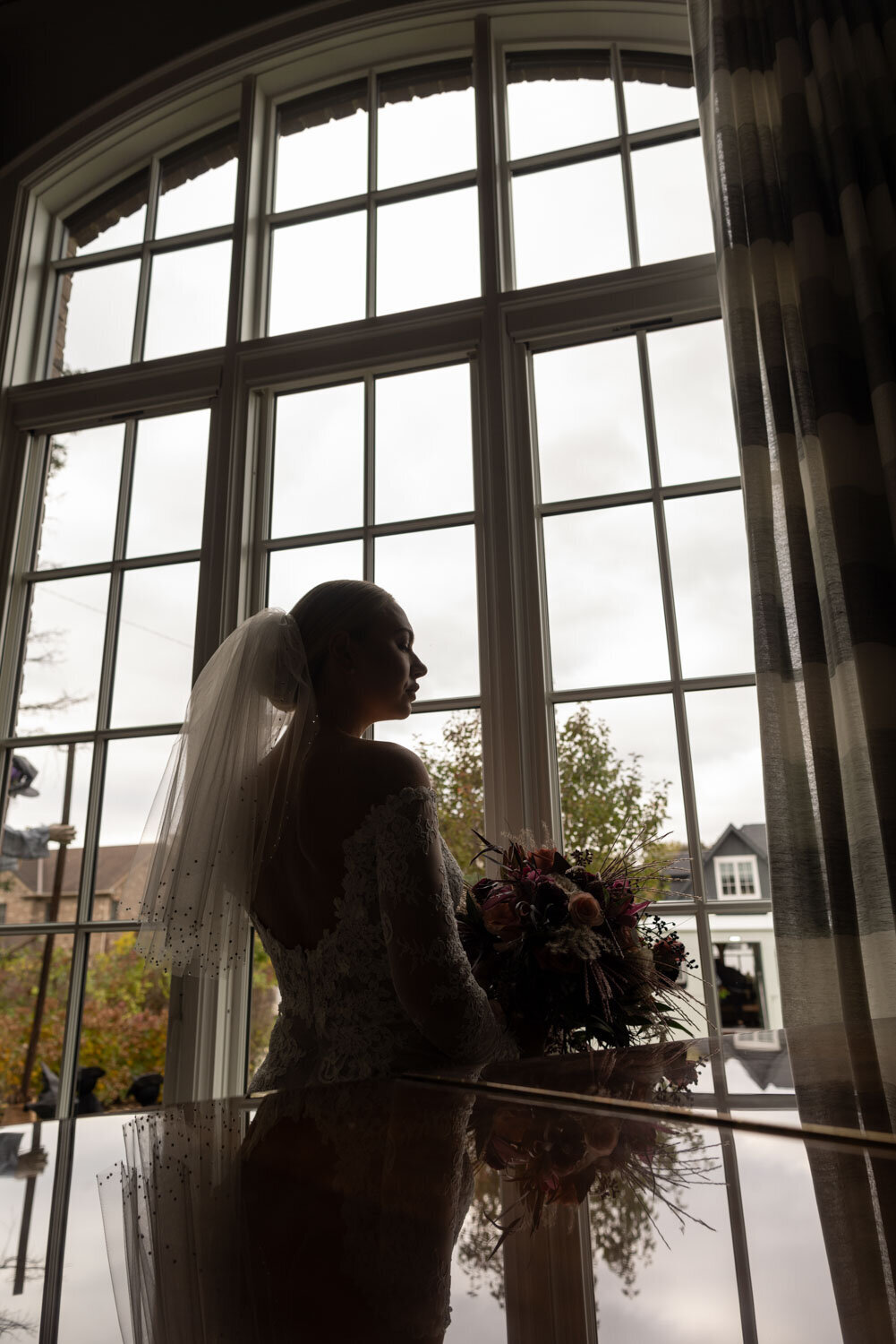 A bride is standing in front of a window holding a bouquet of flowers