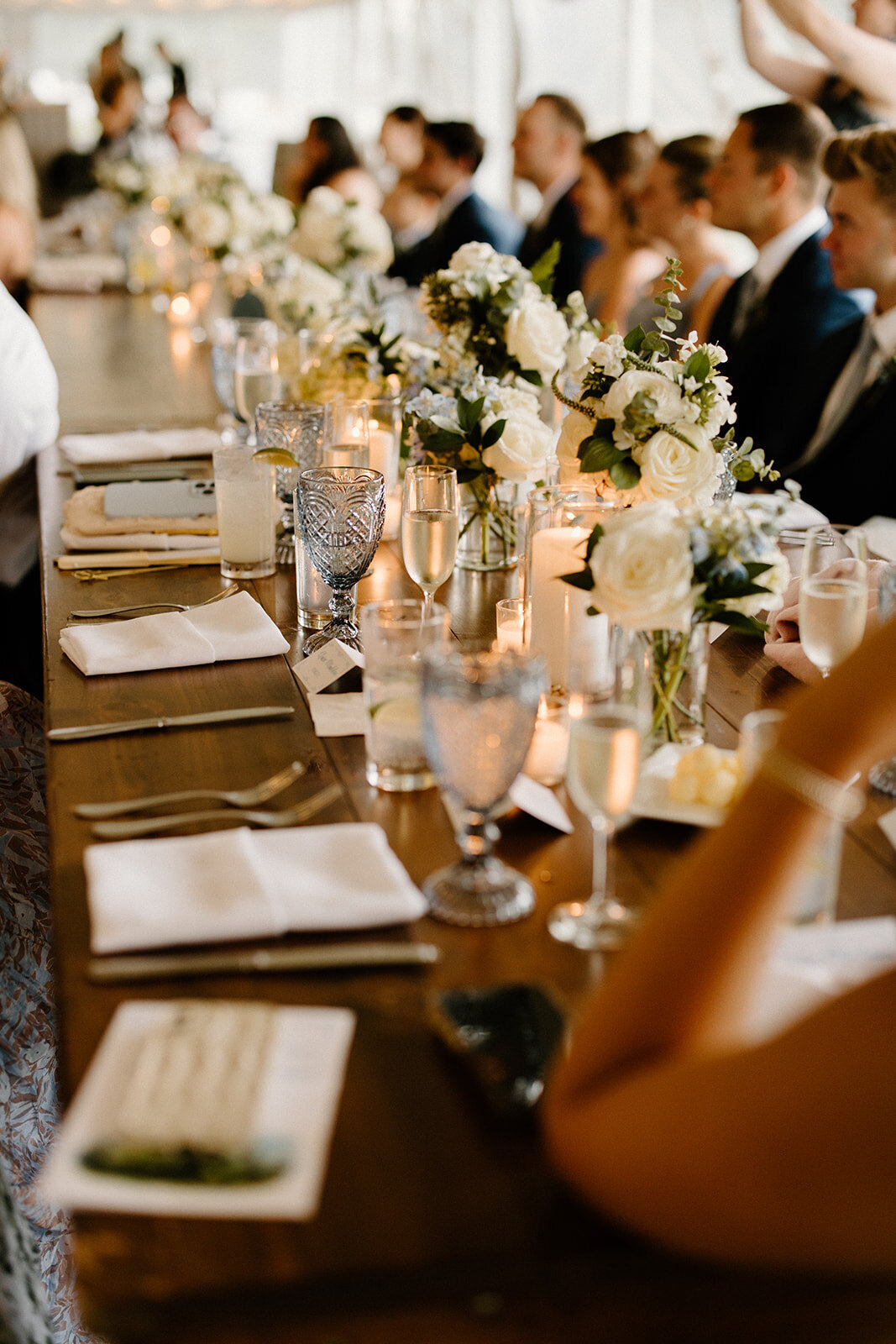 A table setting photo with wedding guests seated around. White flowers and simple design.