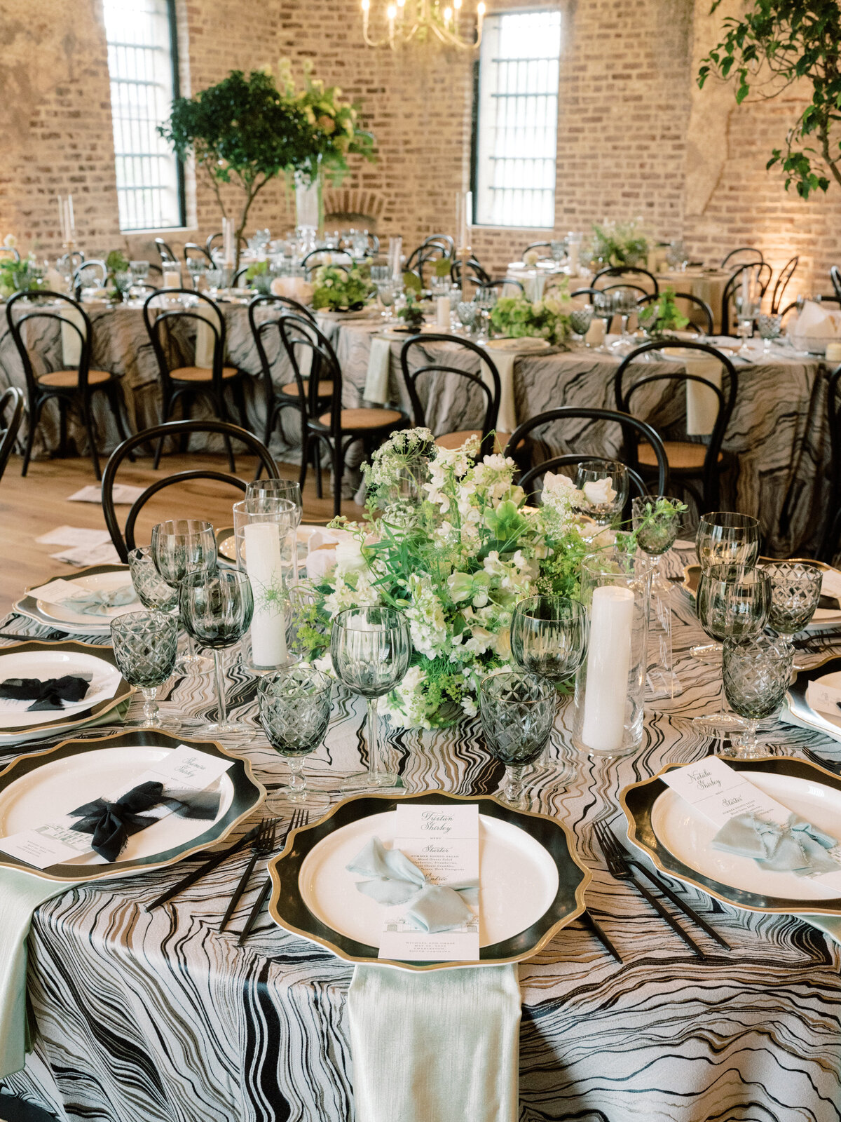 This image features a sophisticated wedding reception table arrangement showcasing elegant plates, exquisite floral centerpieces, and thoughtfully placed glassware.