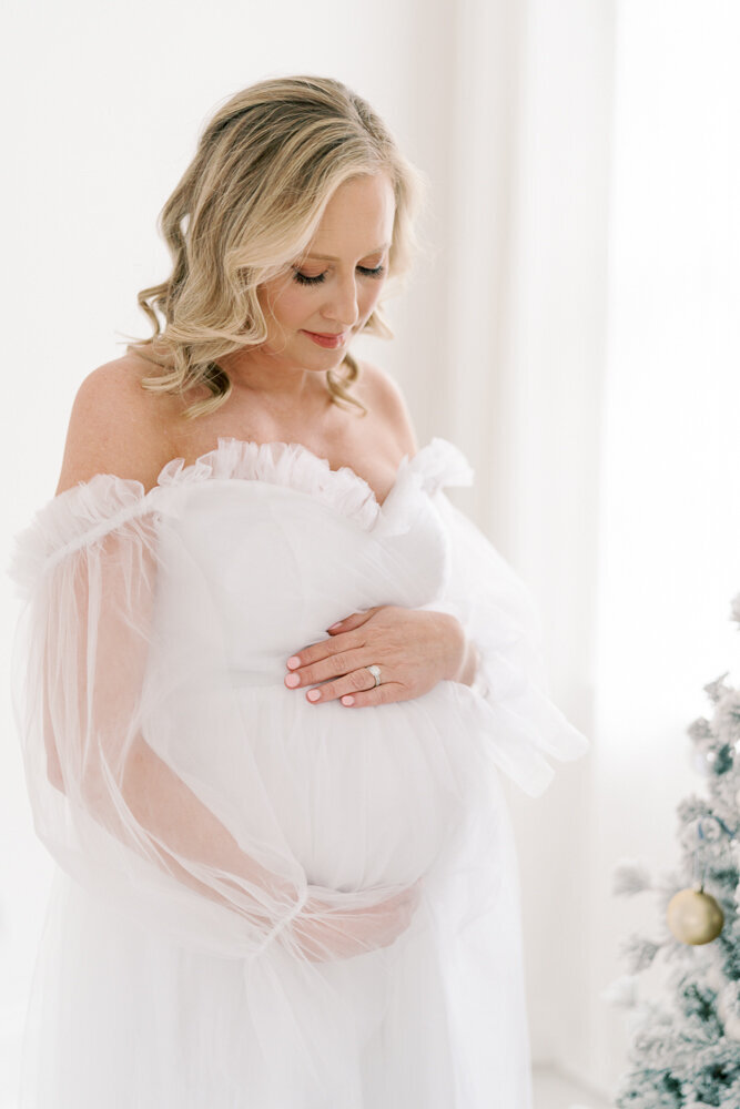blonde-expecting-mom-looking-down-at-belly-in-white-gown